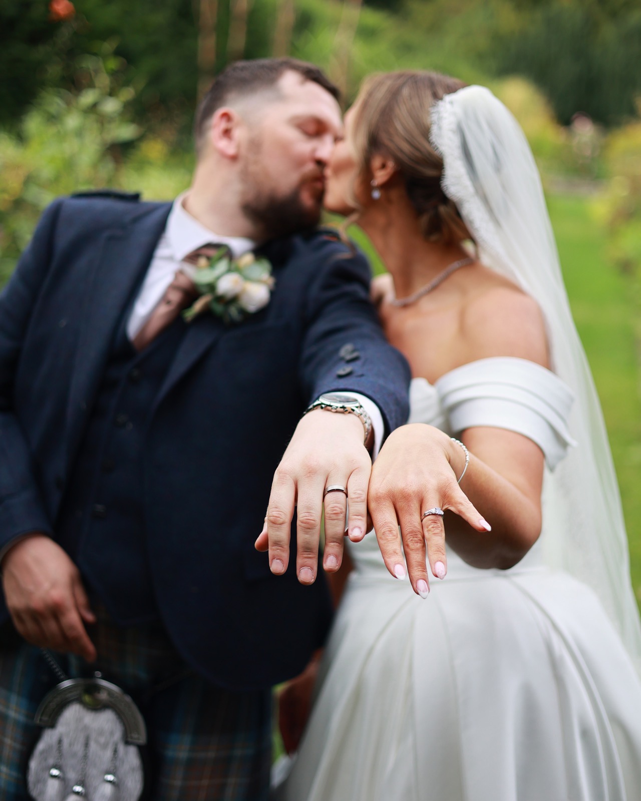 Bride and groom kissing while both showing off their wedding rings to the camera