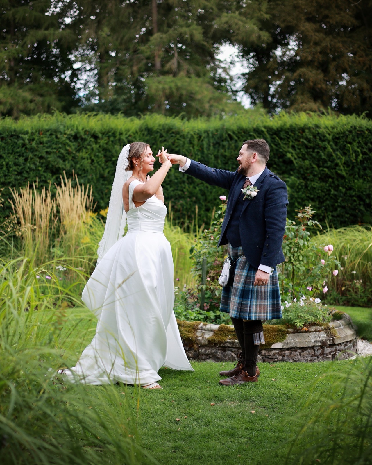 Groom twirling the bride beside a rose garden bed
